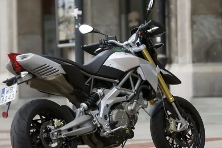 Srebrno-czarny motocykl Aprilia Dorsoduro 750 z żółtymi lagami, gotowy do jazdy po miejskich ulicach.