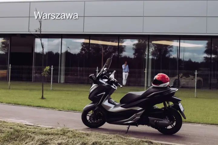 Elegancki skuter Honda Forza 300 zaparkowany przed budynkiem z napisem "Warszawa". Czerwony kask leży na siedzeniu.