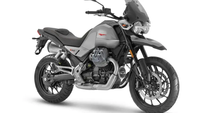 Srebrny motocykl Moto Guzzi V85 TT z czarnym siedzeniem i przyciemnianą szybą, gotowy na przygodę.