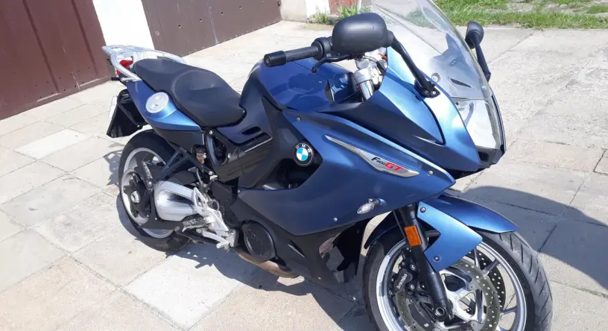Błękitny motocykl BMW F800 GT stoi na chodniku przed garażem.