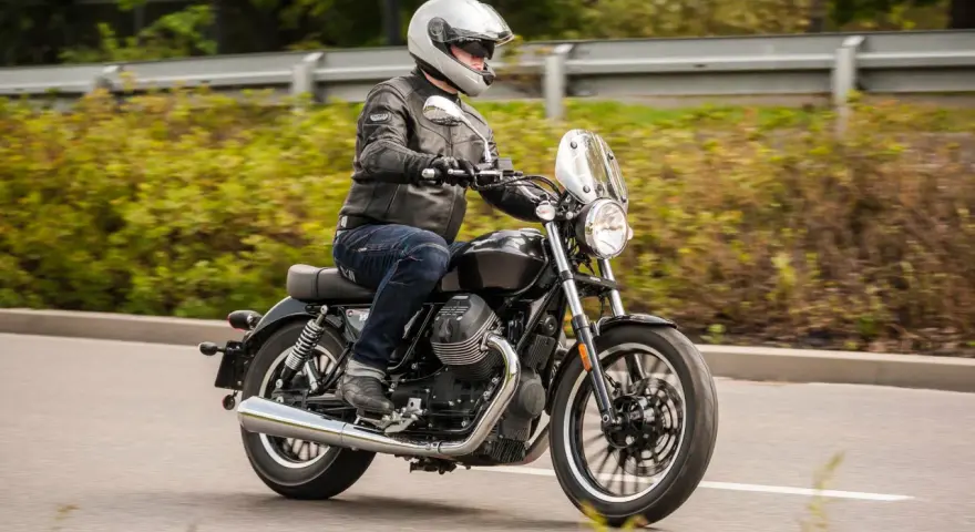 Motocyklista w kasku i skórzanej kurtce jedzie na stylowym motocyklu Moto Guzzi V9.
