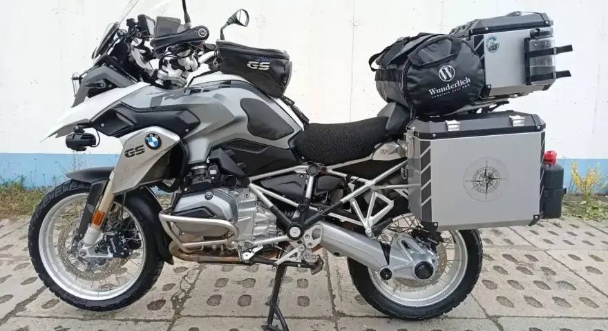 Srebrny motocykl BMW R1200GS z kuframi i torbą na bak. Wady tego modelu to m.in. wysoka cena i skomplikowana elektronika.