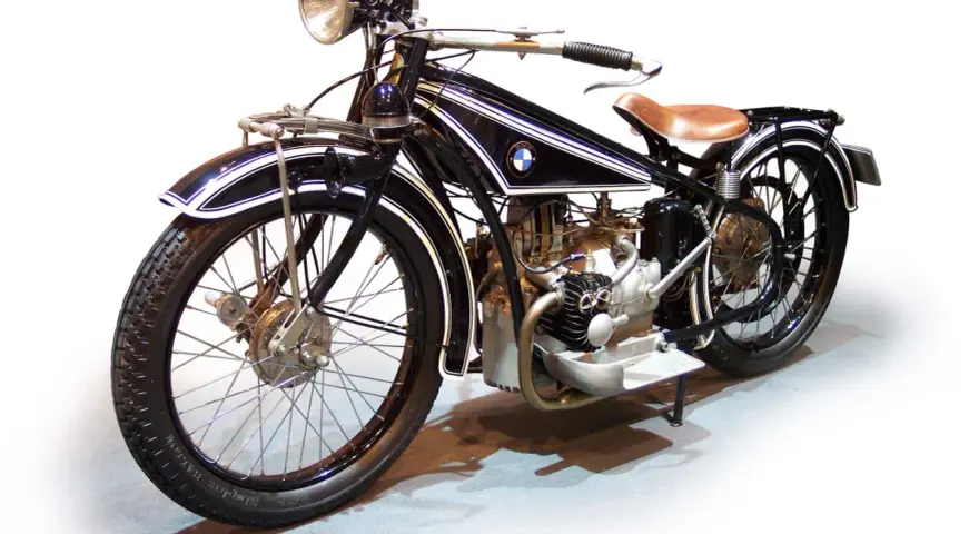 Klasyczny motocykl BMW z lat 20. XX wieku, czarny z białymi pasami, z brązowym siodłem. Ikona historii BMW.