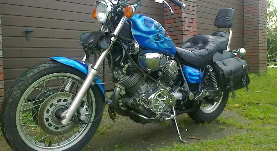 Błękitny motocykl Yamaha Virago 1100 z płomieniami, skórzanymi sakwami i oparciem. Wady i zalety tego klasyka do rozważenia przed zakupem.