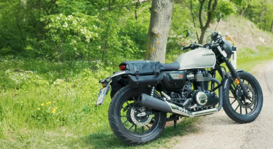 Stojący na poboczu, w otoczeniu zieleni, motocykl Honda GB350 z sakwami gotowy na podróż.