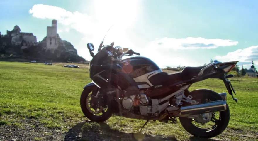 Motocykl na tle zamku na skale i zielonej łąki.