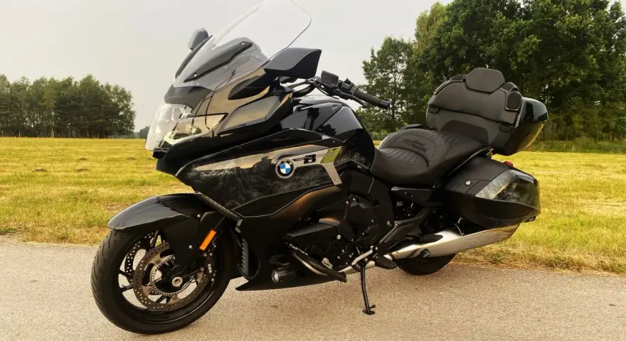 Czarny motocykl BMW K1600 Grand America z kuframi, gotowy na daleką podróż pośród zielonych pól i drzew.