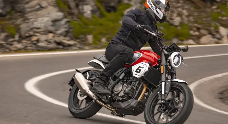 Motocyklista w kasku jedzie czerwonym motocyklem po krętej drodze. Idealny motor na początek przygody z jazdą.