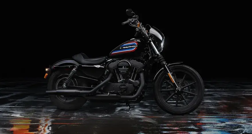 Czarny Harley-Davidson Iron 1200 z kolorowym paskiem na baku, stojący na mokrej, błyszczącej nawierzchni.