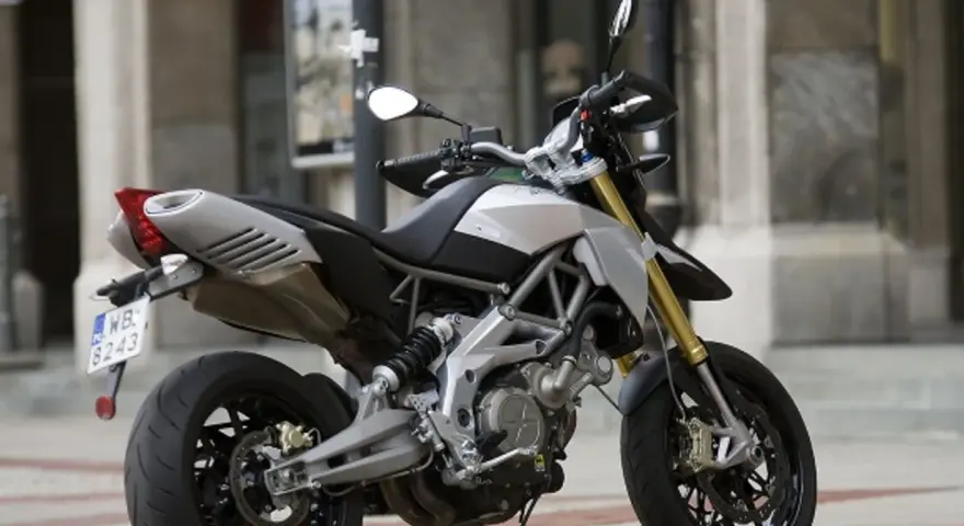Srebrno-czarny motocykl Aprilia Dorsoduro 750 z żółtymi lagami, gotowy do jazdy po miejskich ulicach.