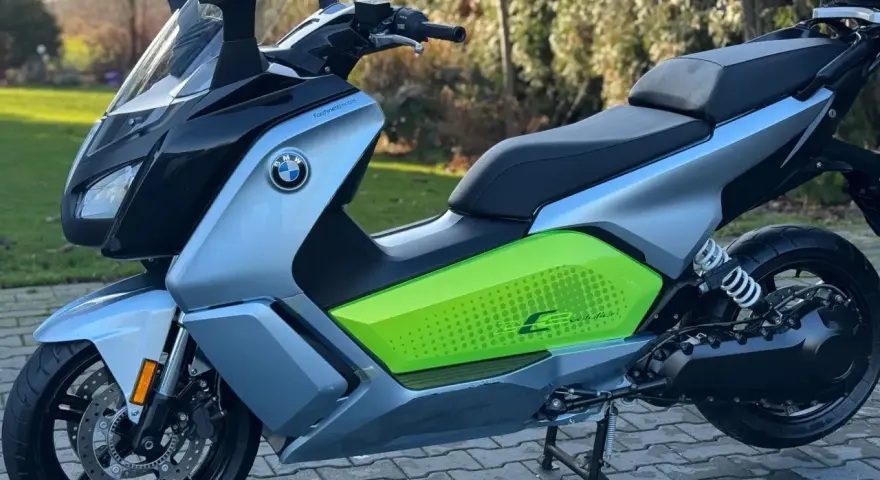 Srebrno-czarny skuter elektryczny BMW C Evolution z zielonym akcentem i napisem "C Evolution" na boku, stojący na chodniku.