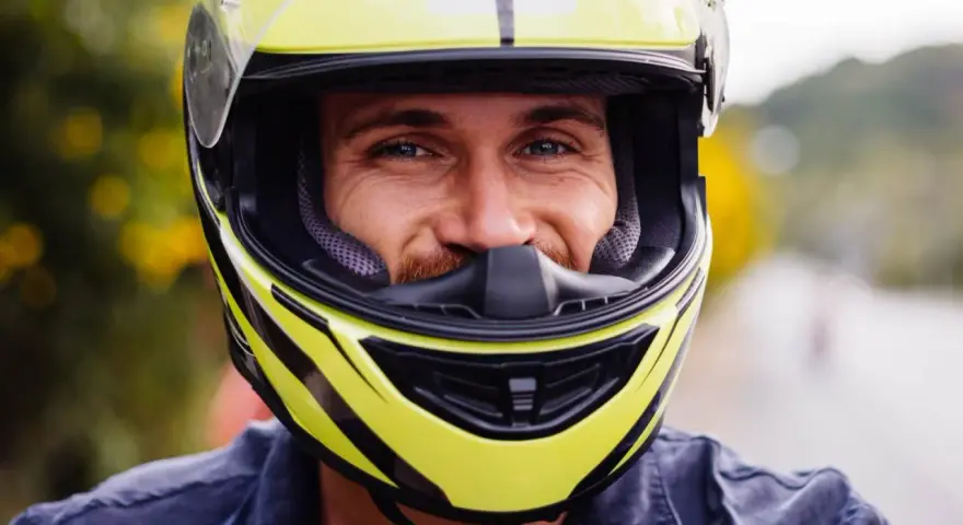 Uśmiechnięty mężczyzna w żółtym kasku motocyklowym z czarnymi elementami.