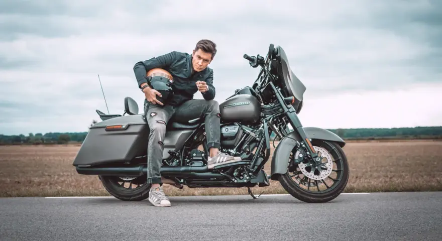 Mężczyzna w czarnej kurtce i podartych jeansach siedzi na motocyklu Harley-Davidson Street Glide, trzymając kask.