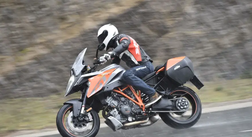 Motocyklista w kasku i kombinezonie śmiga na KTM Super Duke 1290 GT w deszczu.