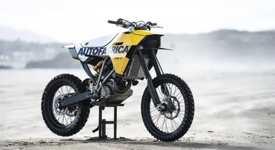 Żółto-biały motocykl customowy Autofabrica Type 17, bazujący na BMW G450X, stoi na plaży.