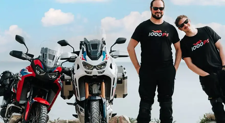 Dwóch mężczyzn w koszulkach 1000PS obok motocykli Honda Africa Twin.