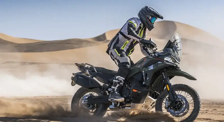 Motocyklista w pełnym rynsztunku szaleje na pustyni na swoim KTM 790 Adventure, wzbijając tumany piasku.