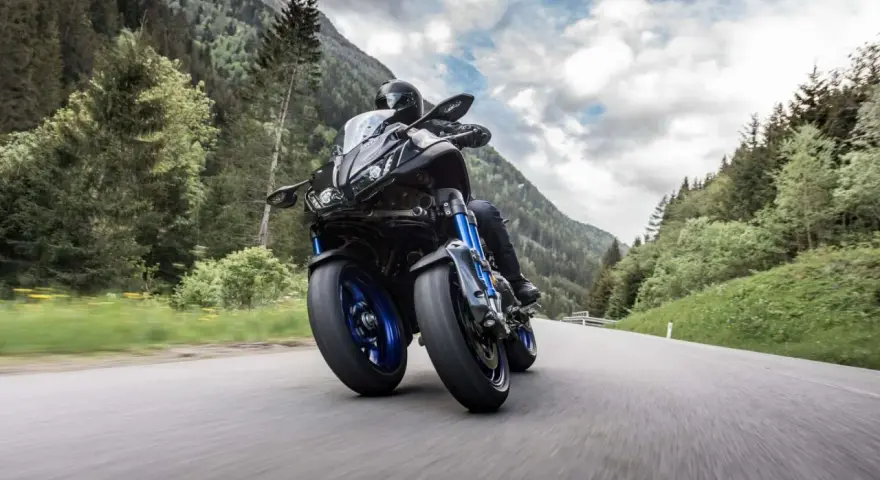 Motocyklista na Yamaha Niken pokonuje górską drogę, otoczony zielonymi lasami i skalistymi szczytami.