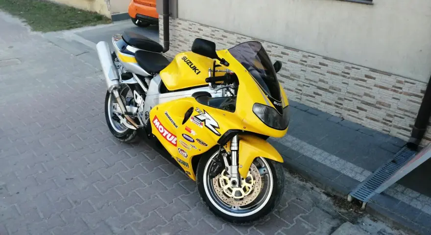 Żółty motocykl Suzuki TL1000R z naklejkami sponsorów, zaparkowany na chodniku.