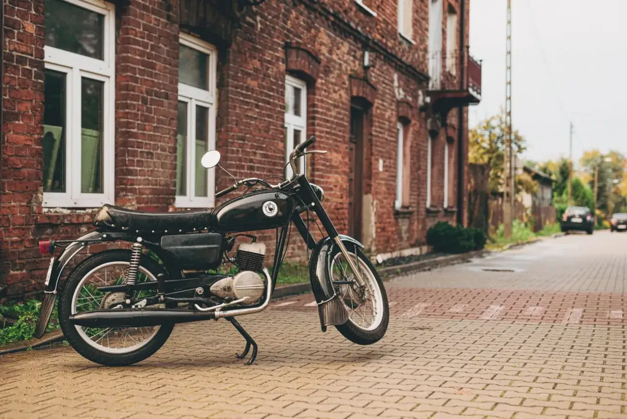 Czarny motocykl WSK 125, z charakterystycznym silnikiem, zaparkowany na brukowanej ulicy przed starą ceglaną kamienicą.