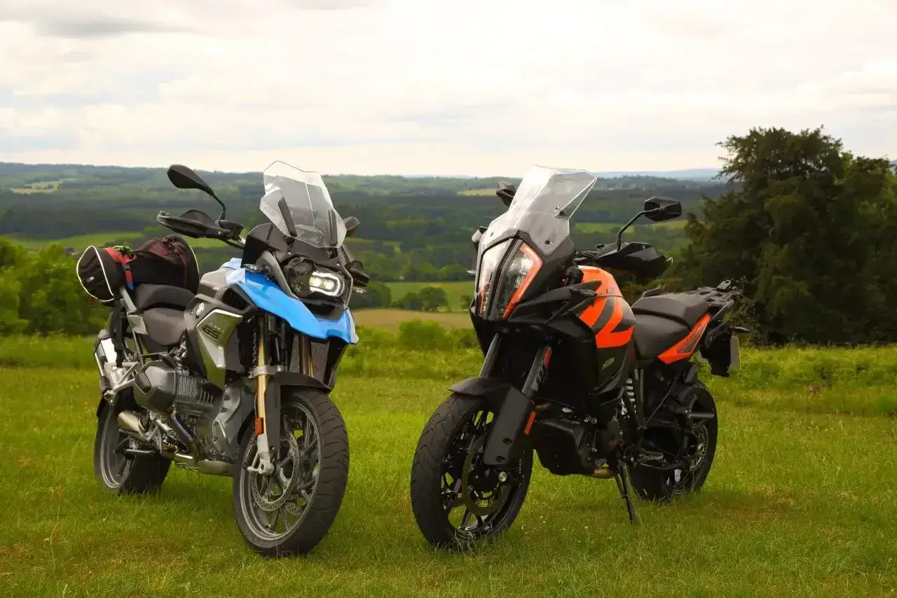 Dwa motocykle turystyczne, w tym pomarańczowy KTM 1290 Super Adventure, stoją na trawie. Poznaj jego dane techniczne.