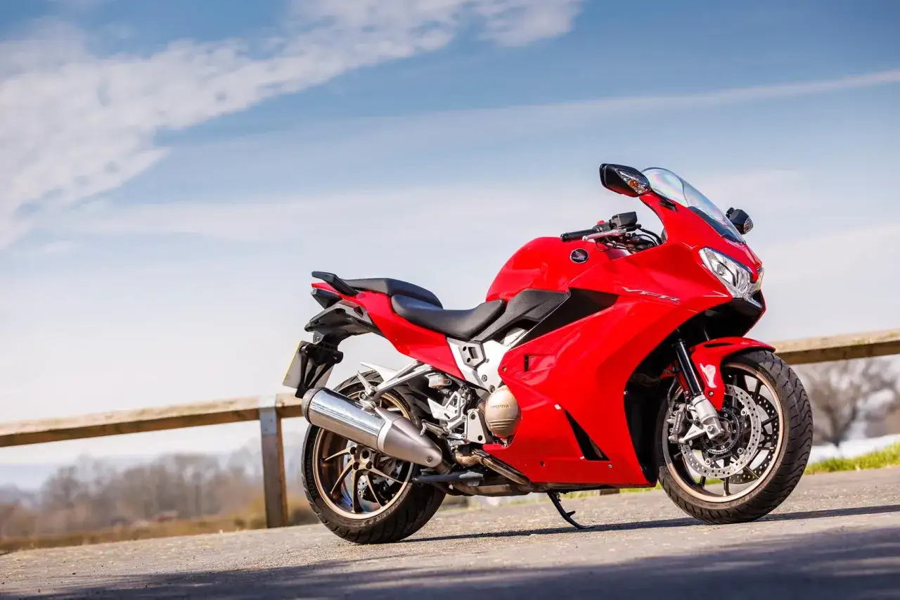 Lśniąca, czerwona Honda VFR 800 na tle błękitnego nieba z chmurami. Motocykl stoi na drodze, gotowy do podróży.
