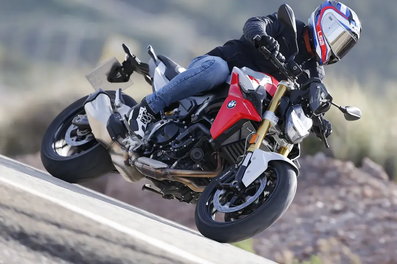 Motocyklista w kasku pochyla się na zakręcie na sportowym motocyklu BMW F900R.