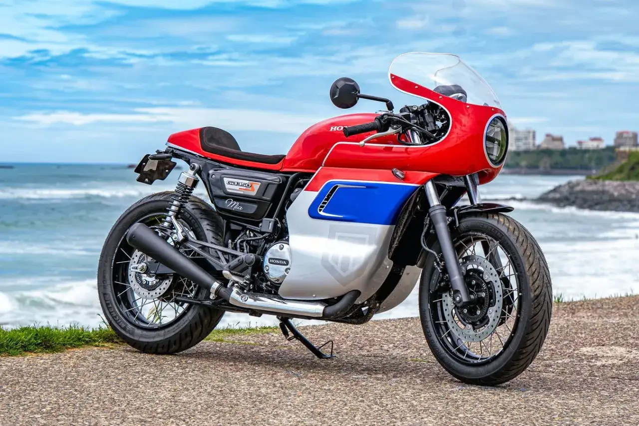 Stylowy motocykl Honda GB350 w kolorach czerwonym, białym i niebieskim, zaparkowany nad morzem.