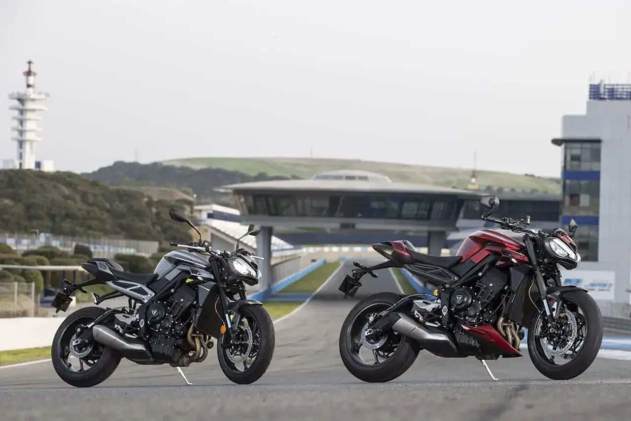 Dwa motocykle Triumph Street Triple, jeden czarny, drugi czerwony, stoją na torze wyścigowym.