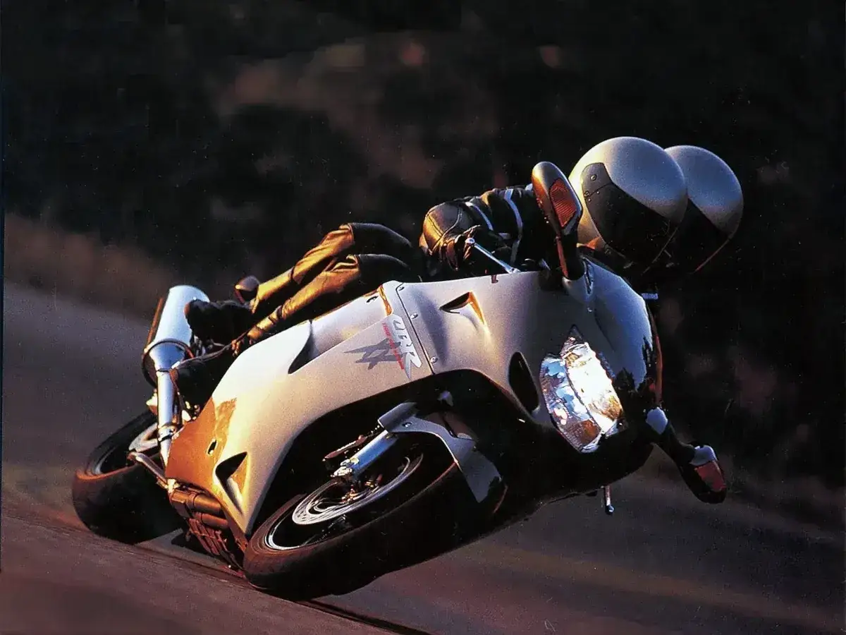 Motocyklista w skórzanej kurtce pochyla się nad sportowym motocyklem Honda CBR1100XX, pokonując zakręt.