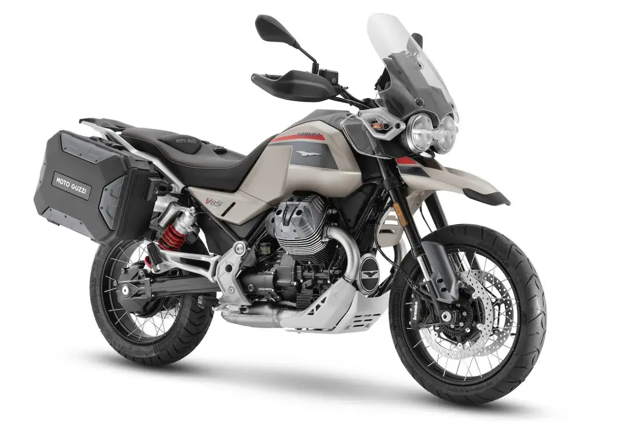 Beżowy motocykl Moto Guzzi V85 z kuframi, gotowy na przygodę.