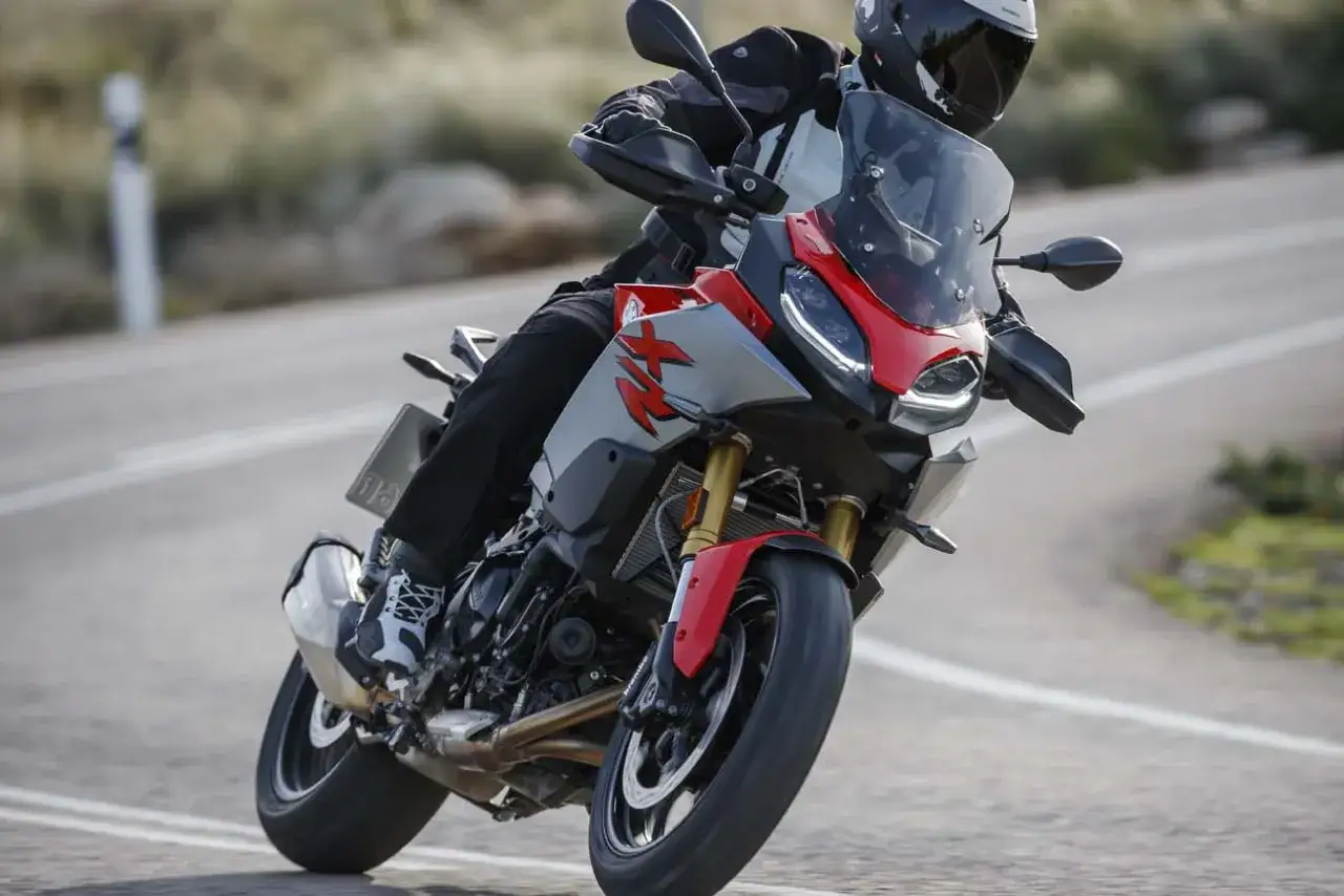 Motocyklista w kasku pochyla się na zakręcie na drodze, prowadząc sportowo-turystyczny motocykl BMW F900XR.