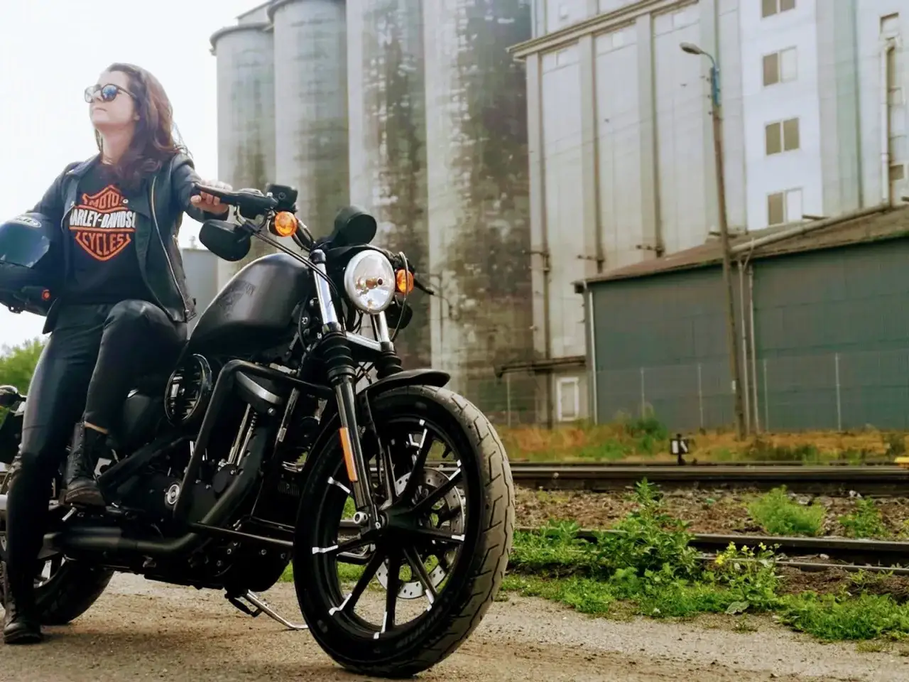 Kobieta w skórzanej kurtce siedzi na czarnym motocyklu Harley Davidson Sportster 883, gotowa do jazdy.