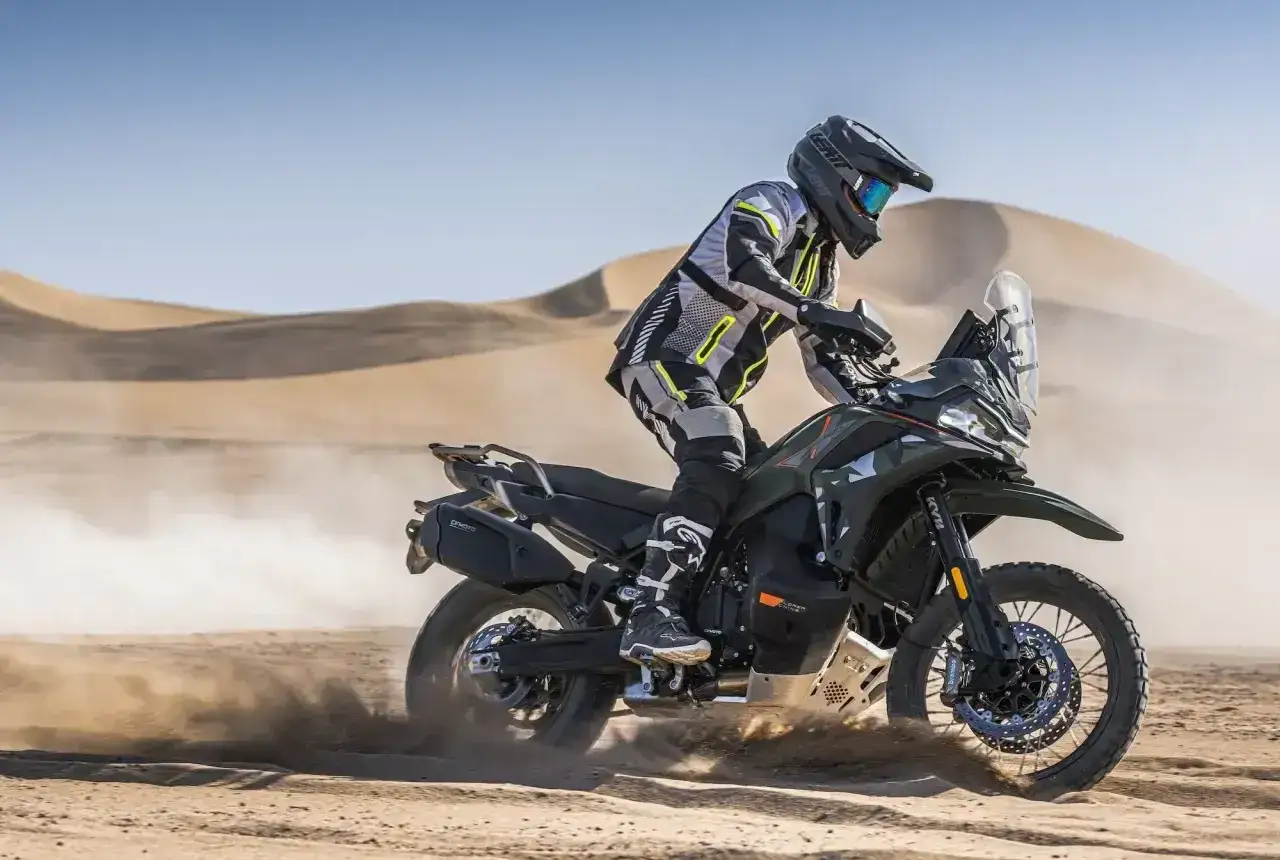 Motocyklista w pełnym rynsztunku szaleje na motocyklu KTM 790 Adventure po piaszczystych wydmach.