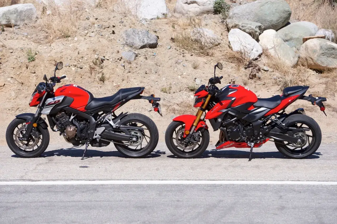 Dwa czerwone motocykle, Honda i Suzuki GSX, stoją obok siebie na tle skalistego zbocza.