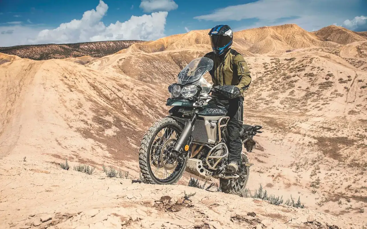 Motocyklista na motocyklu Triumph Tiger 800 XC w pustynnym krajobrazie. Dane techniczne tego modelu pozwalają na takie wyprawy.