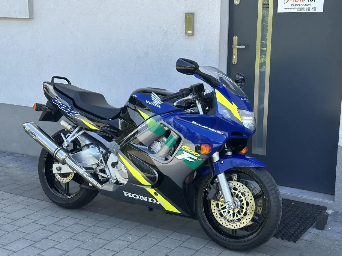 Niebieski motocykl Honda CBR 600 F3 z żółtymi akcentami, zaparkowany przed drzwiami.