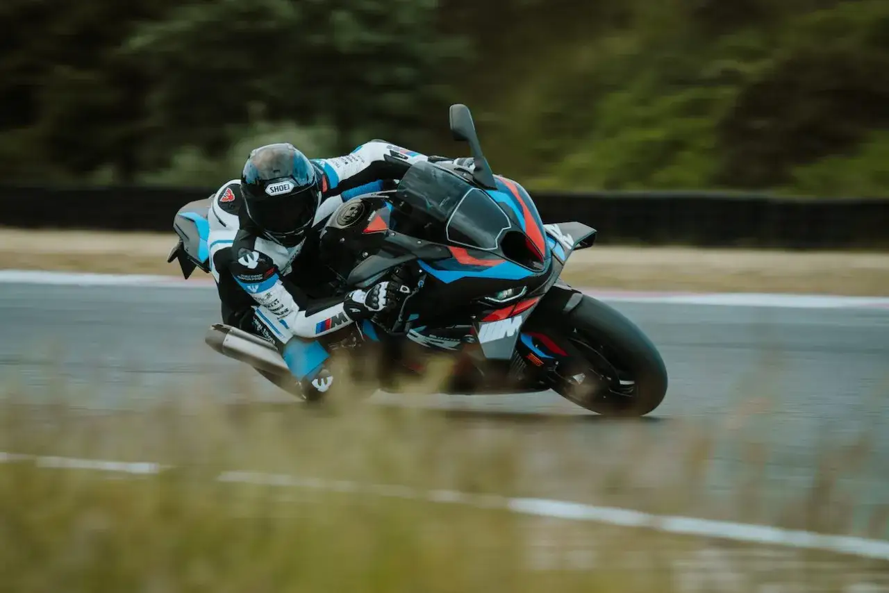 Motocyklista w kombinezonie ściga się na torze na sportowym motocyklu BMW S1000R, pochylając się w zakręcie.