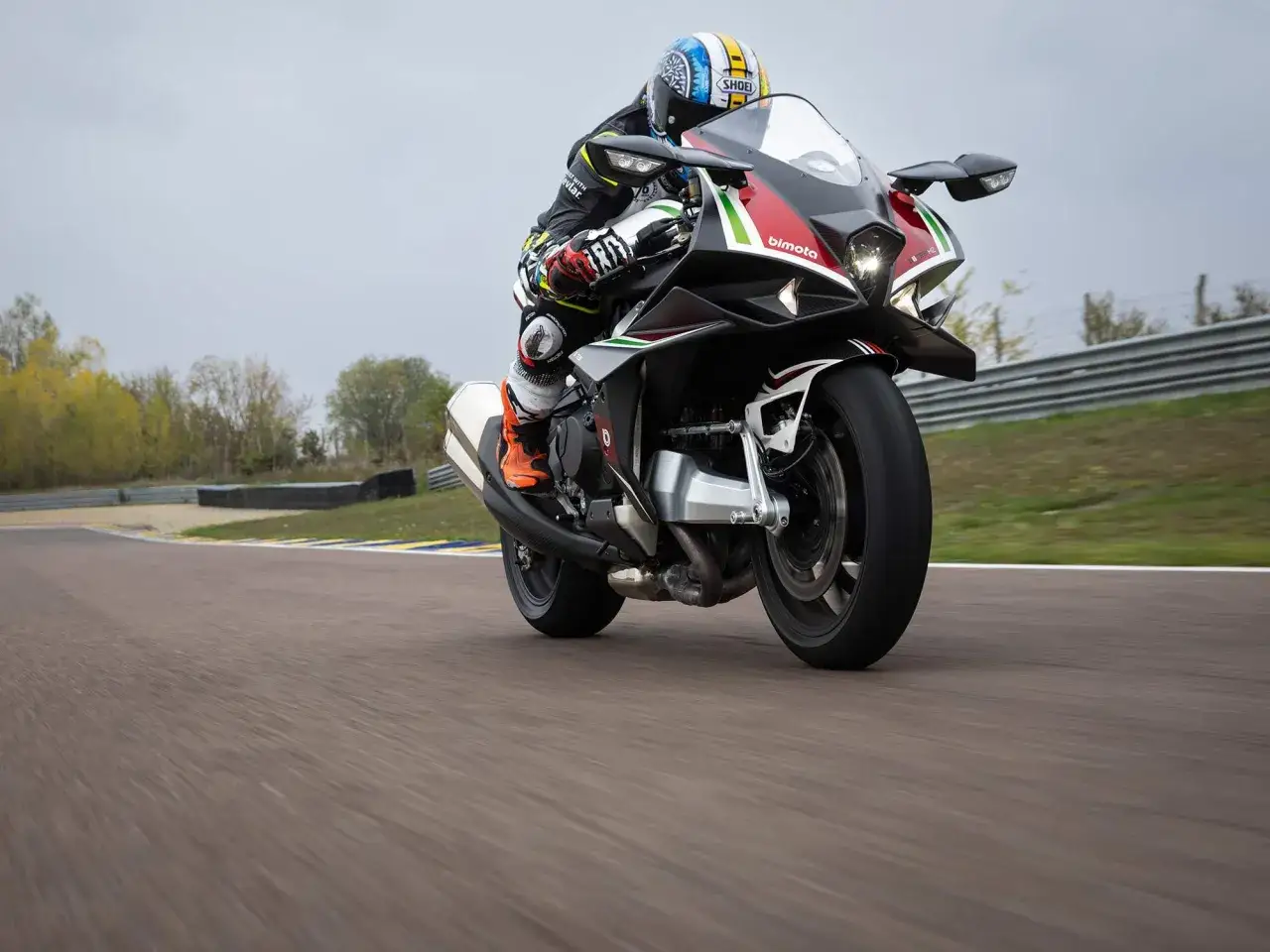 Motocyklista na torze ściga się na sportowym motocyklu Bimota Tesi H2, który wyróżnia się agresywnym designem i kolorystyką.