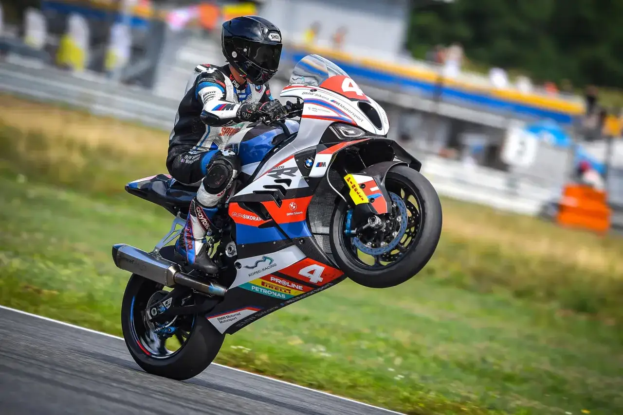 Motocyklista na torze wykonuje wheelie na sportowym motocyklu BMW M1000R. Maszyna w barwach BMW Motorsport z numerem 4.