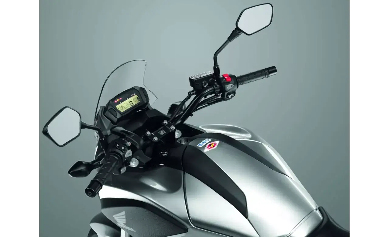Szara Honda NC 700, widok na kierownicę i zbiornik paliwa. Cyfrowy wyświetlacz pokazuje prędkość. Dane techniczne dostępne dla tego modelu.