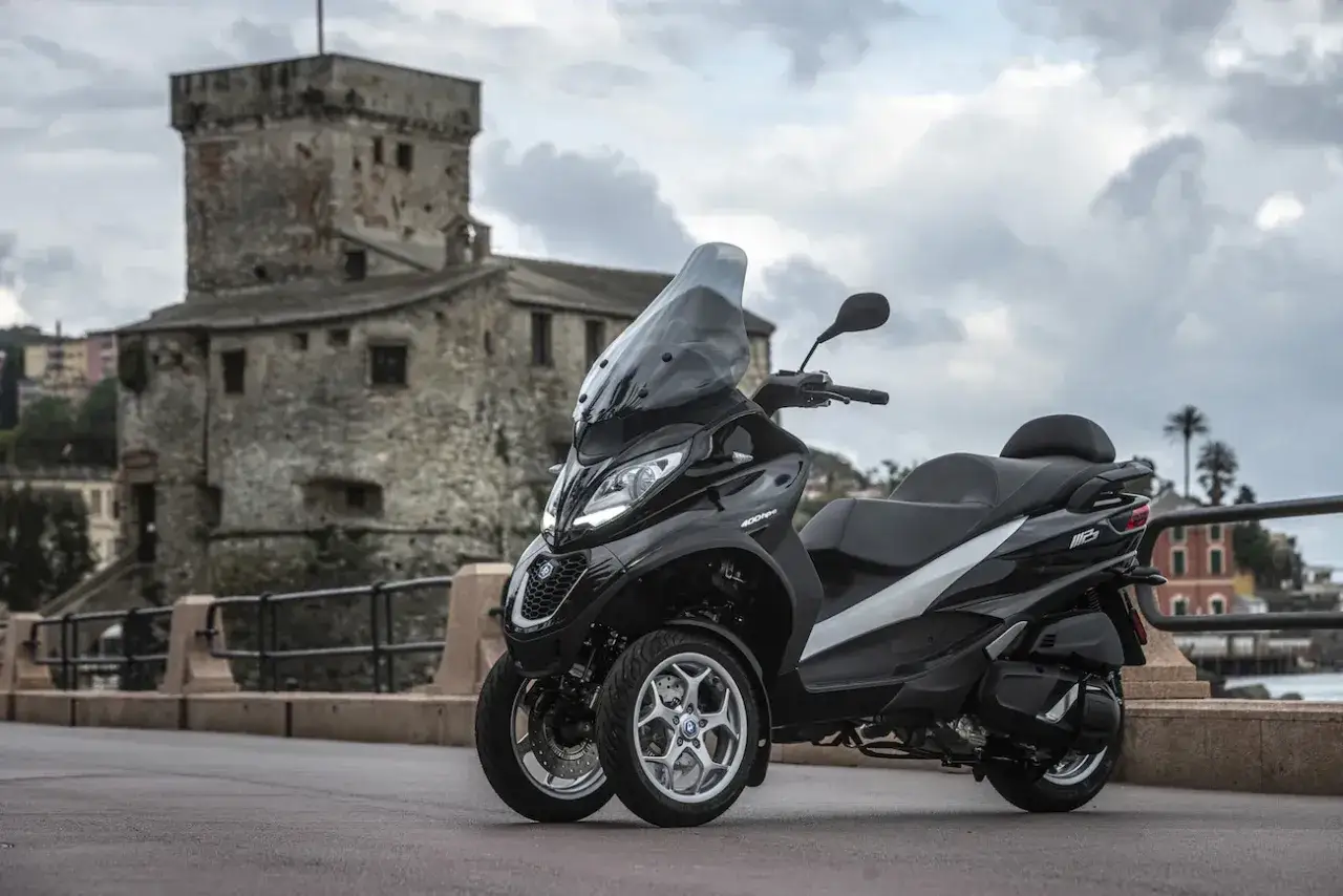Czarny Piaggio MP3 400, z jego imponującymi danymi technicznymi, zaparkowany na tle zabytkowej wieży i morza.