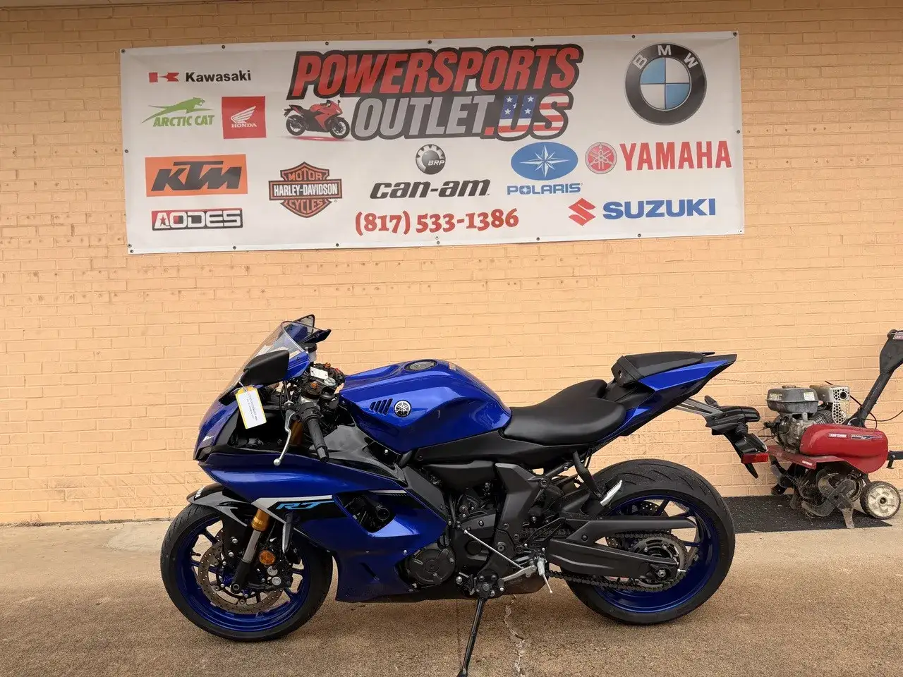 Niebieski motocykl Yamaha R7, idealny do poznania jego yamaha r7 dane techniczne. Obok kosiarka.