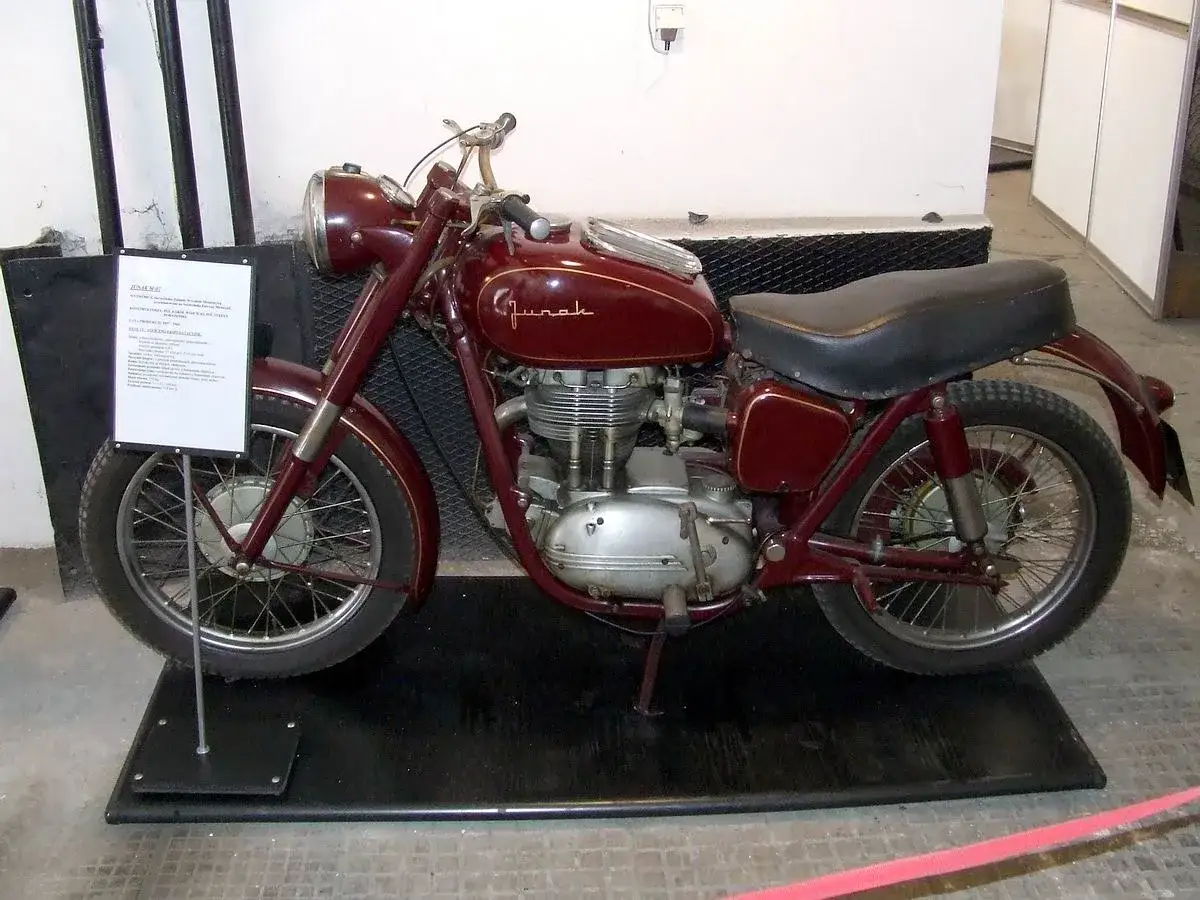 Czerwony motocykl Junak z lat 50. XX wieku, stojący na czarnej macie.