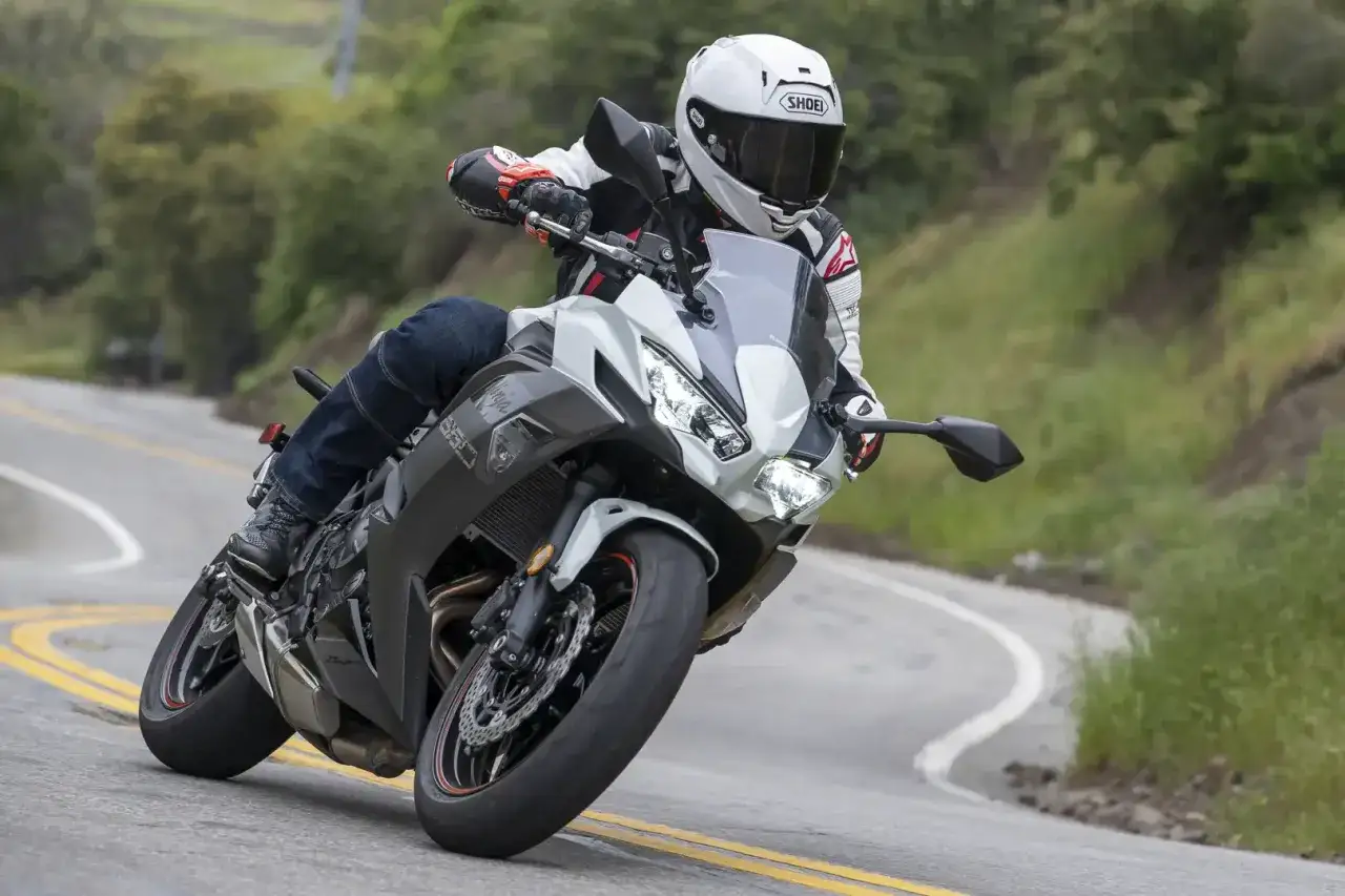 Motocyklista w białym kasku i kombinezonie pochyla się na zakręcie na szosie, prowadząc szaro-białego Kawasaki Ninja 650. Dane techniczne tego modelu są imponujące.
