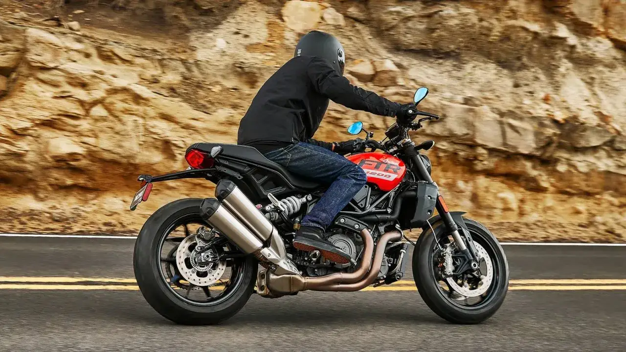 Motocyklista na czerwonym Indian FTR 1200 przemierza krętą drogę wśród skalistych zboczy.