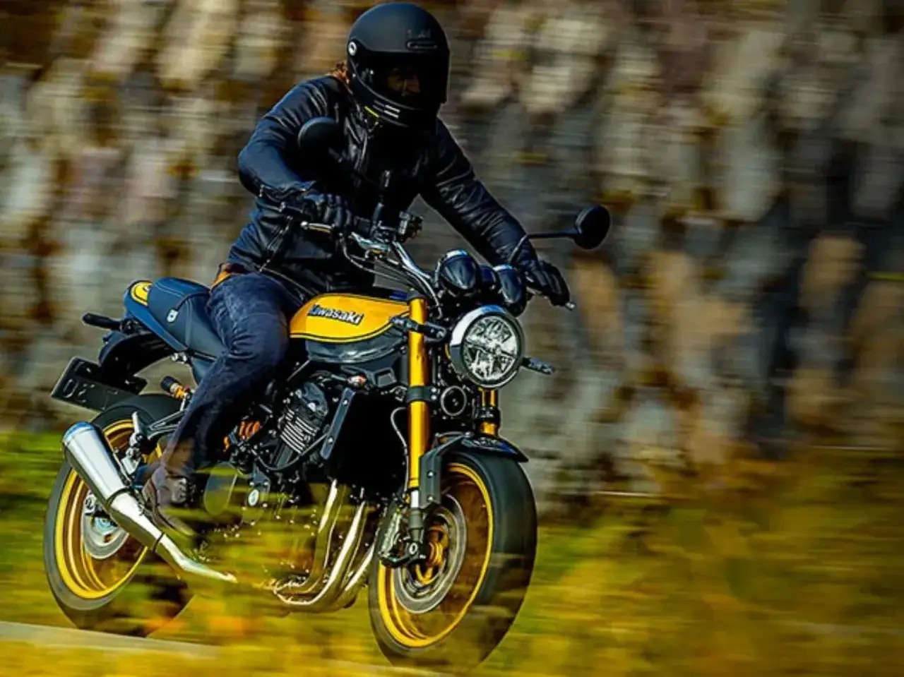 Motocyklista w czarnej kurtce i kasku pędzi na żółto-czarnym Kawasaki Z900RS.