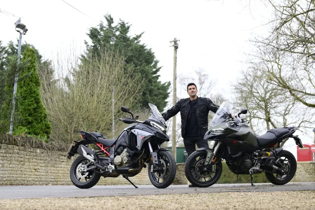 Mężczyzna w czarnej kurtce stoi między dwoma motocyklami Ducati Multistrada. Jeden jest czarny, drugi oliwkowy.