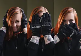 Kobieta z rudymi włosami w czarnych rękawicach motocyklowych zakrywa twarz.