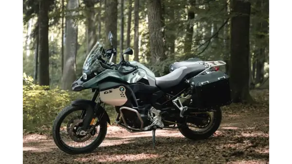 Zielony motocykl BMW F900GS z kuframi, gotowy na przygodę w lesie.